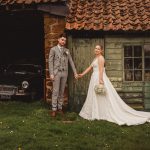 Bride and groom holding hands by rustic garage.