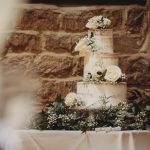 Three-tier wedding cake with white roses and greenery.