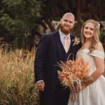 Bride and groom smiling in garden setting.