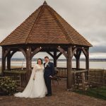 Couple under wooden gazebo on cloudy wedding day.