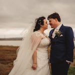 Bride and groom embracing outdoors, overcast sky.