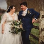 Bride and groom smiling outdoors by a fence.