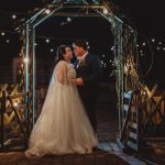 Couple at night under fairy-lit archway.