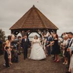 Wedding guests celebrate with confetti under wooden gazebo.