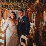 Smiling couple in wedding attire inside rustic venue.