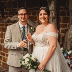 Bride and groom smiling with drinks and bouquet.