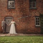 Couple holding hands outside brick cottage.