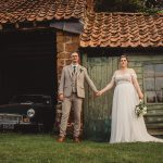 Bride and groom holding hands by rustic building.