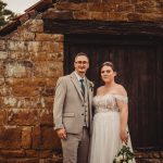 Bride and groom by rustic stone building.