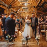 Bride walking down barn wedding aisle with guests.