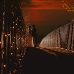 Couple silhouetted on illuminated bridge at sunset.