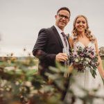 Smiling couple at outdoor wedding with bouquet.