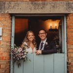 Smiling couple at rustic wedding venue window.