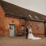 Bride and groom by rustic brick building.