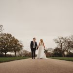 Newlyweds walking on road, autumn trees surrounding them.