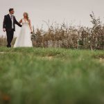 Bride and groom walking on grassy path.