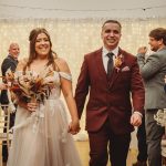 Smiling couple walks down the aisle, wedding backdrop.