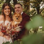 Couple with dog in autumn wedding attire.