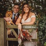 Couple in wedding attire with dog on gate