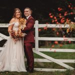 Bride and groom with dog by garden gate.