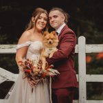 Bride and groom pose with dog by a gate.