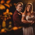 Smiling couple in wedding attire, autumn background.