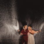 Couple celebrating with champagne spray at night.