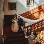 Bride walking down staircase with father, elegant setting.