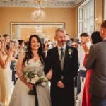 Bride and groom walking down aisle, guests applauding.