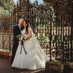 Bride and groom by ornate iron gate.