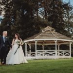 Bride and groom walking by garden gazebo.