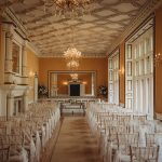 Elegant wedding ceremony room with chandeliers and chairs.