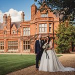 Couple in wedding attire outside historic red-brick manor.