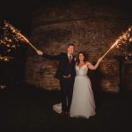 Couple holding sparklers during night wedding celebration.