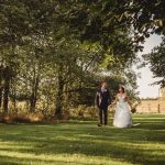 Bride and groom walking through a leafy garden.