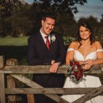 Bride and groom by a wooden gate outdoors.