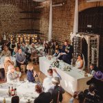 Wedding speech in rustic venue, love sign visible.