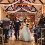 Newlyweds walking down aisle, guests applauding.