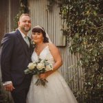 Bride and groom pose by rustic wall with ivy.