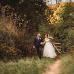 Bride and groom walking in lush countryside.