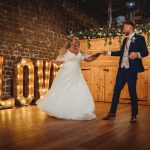 Couple's first dance beside illuminated LOVE sign.