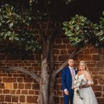 Bride and groom under tree against brick wall