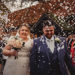 Smiling newlyweds walking through confetti shower.