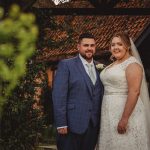 Happy couple in wedding attire outside rustic building.