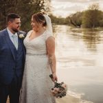 Bride and groom by riverside at sunset