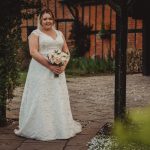 Bride in lace gown holding flower bouquet outdoors