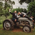 Two men in suits on vintage tractor, outdoors.