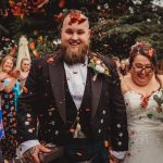 Bride and groom showered with confetti, surrounded by guests.