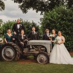 Wedding party posing with vintage tractor outdoors.