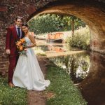 Bride and groom by canal under bridge.